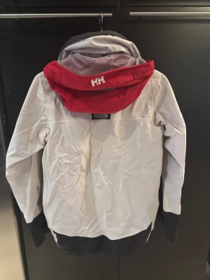 Helly Hansen vit regnjacka  - Snygg vit regnjacka från Helly Hansen med röda och svarta detaljer, stor krage i grått fleece och praktisk huva. Storleken är xs, hör av er vid minsta fundering 💭 🤩🤩