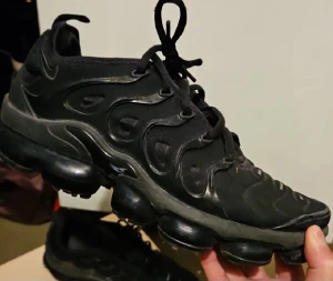 Nike Vapormax svarta sneakers - Svarta Nike Vapormax sneakers med unik bubblig sula och snygga vågformade detaljer på sidan. Skorna har snörning och är tillverkade i syntetmaterial med mesh för extra komfort. Perfekt för dig som gillar sportig och modern stil.