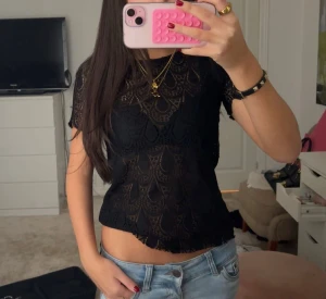 Svart spetsblus med kort ärm - Säljer en svart blus i spets med korta ärmar och snyggt mönster. Blusen är lätt transparent och har en rund halsringning samt vågig kant nedtill. Perfekt för dig som gillar detaljer och vill ha en cool look.