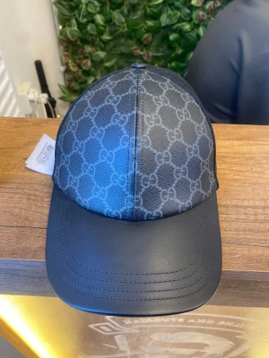 Gucci keps - Snygg svart keps från Gucci med klassiskt GG-mönster på framsidan. Skärmen är i svart skinn och sidorna har mesh för extra ventilation. Justerbar baktill för perfekt passform. Perfekt för dig som vill ha en lyxig streetstyle-look. KVITTO, BOX, PÅSE ALLT FINNS MED. Pris kan diskuteras vid snabbaffär ett riktigt bra pris. Använt 1-2 gånger bara säljs pga att jag inte använder keps mer.