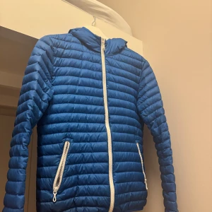 Blå pufferjacka från Colmar - Säljer en snygg blå pufferjacka från Colmar. Jackan har en dragkedja framtill och två praktiska fickor med dragkedjor. Perfekt för kyligare dagar med sin quiltade design och långa ärmar. Huvan ger extra skydd mot väder och vind. passar någon som är cirka 165/xs skick 8/10