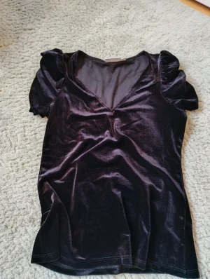 Svart sammetsblus med puffärm Kappahl - Snygg svart blus från Kappahl i mjuk sammet. Modellen har korta puffärmar och en djup v-ringning framtill. Perfekt för dig som gillar en stilren look med lite extra lyxig känsla. Passar dig som vill ha något som sticker ut men ändå är enkelt att matcha. Nästan helt oanvänd.