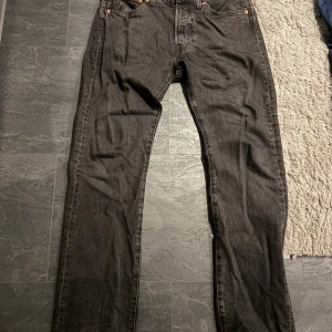 Levi's 501 gråa jeans W31 L32 - Gråa Levi's 501 jeans med klassisk rak passform och fem fickor. Jeansen har en snygg mörk tvätt, knappgylf och ikonisk läderpatch bak i midjan. Perfekta för dig som gillar tidlös stil och vill ha ett par jeans som funkar till allt.