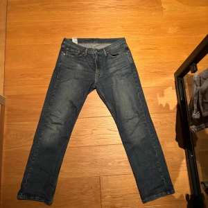 Levi's 514 blå jeans straight fit - Säljer ett par klassiska Levi's 514 jeans i mörkblå tvätt med straight fit. Jeansen har fem fickor, orangea sömmar och en snygg läderpatch bak. Perfekt passform och tidlös stil för dig som gillar jeans med lite mer rakt snitt.