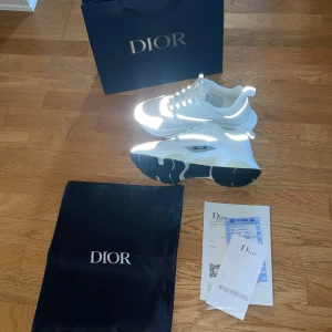  vita Dior b22 skor - Säljer ett par feta chunky sneakers från Dior i vitt och grått med svarta detaljer. Skorna har mesh och skinnpaneler, snörning och en rejäl platt sula. Perfekt för dig som vill sticka ut med en lyxig och modern look. Kommer med originalpåse, kvitto och Dior-förpackning.