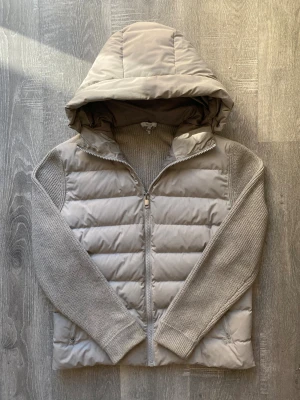 Reiss Jacket Cardigan  - Snygg beige pufferjacka från Reiss. Jackan har stickade ärmar, quiltad kropp och stor huva. Dragkedja framtill och två fickor. Perfekt för kyliga dagar när du vill vara både varm och stilren. Den är i storlek XL men sitter mer som L/XL