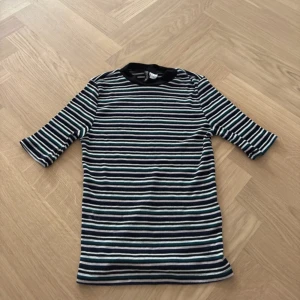 Randig ribbad topp från H&M Divided - Säljer en randig topp från H&M Divided i storlek S. Toppen har svart krage, trekvartsärm och är ribbad med horisontella ränder i svart, vit, blå, grön och ljuslila. Perfekt för dig som gillar färg och mönster. Materialet är mjuk bomull med lite stretch.