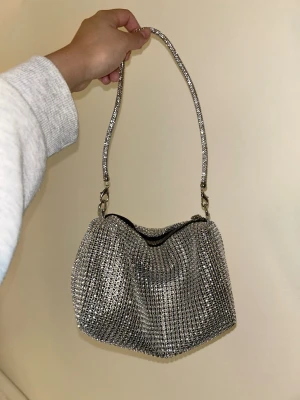 Glittrig silver handväska - Säljer en glittrig handväska i silver. Väskan har ett kort axelband som också är täckt av glitter. Från Shein, skriv om flera bilder önskas 🥰