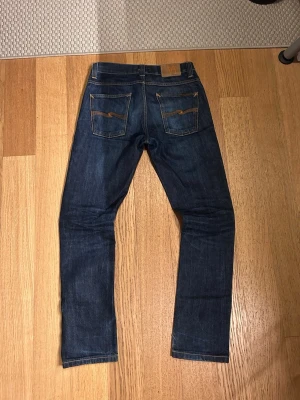 Nudie jeans Grim Tim mörkblå - Säljer ett par super schyssta Nudie jeans i modellen Grim Tim. Jeansen är använda och där med fått snygga slitningar. Inga hål eller lagningar, mycket bra skick. Storlek 30/32. Dom är uppsydda eller något, kan skicka mått på längden ifall det önskas. Hör av dig vid minsta intresse 