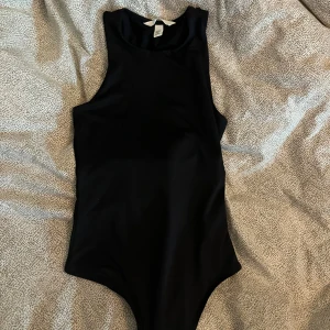 Svart body från H&M - Snygg svart body från H&M i stretchigt material. Modellen har breda axelband och rund halsringning, perfekt att styla till olika outfits. Enkel och stilren design som passar till mycket.