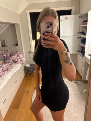 Svart tight kortklänning - En svart, tight kortklänning med korta ärmar och rund halsringning. Klänningen har en enkel och stilren design som framhäver figuren. Perfekt för dig som gillar minimalistisk stil och vill ha en klassisk bas i garderoben. Är i storlek M och köpte den på New Yorker. Har inga skador 