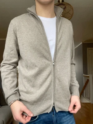 Soft Goat full zip cardigan – strl M - Exklusiv full zip cardigan från Soft Goat i 100% Kashmir. Tröjan är i princip helt ny och i perfekt skick. Minimalistisk och väldigt premium i både känsla och look. Perfekt till både vardag och mer uppklätt.   Skick: Mycket bra skick Storlek: M Färg: Beige  Nypris: 3299 kr
