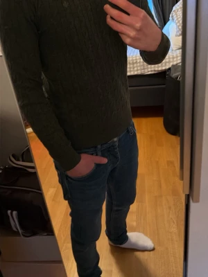 Mörkgrön kabelstickad tröja Morris - Säljer en mörkgrön kabelstickad tröja från Morris med rund halsringning och diskret logga broderad på bröstet. Tröjan har lång ärm och är tillverkad i premium merinoull pris går alltid att pruta