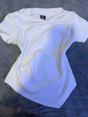 Vit topp med kort ärm - Snygg vit topp med omlottkrage och korta ärmar. Toppen har en figurnära passform och är tillverkad i ett mjukt material som ger en clean och fräsch look. Perfekt att styla med jeans eller kjol för en trendig outfit.