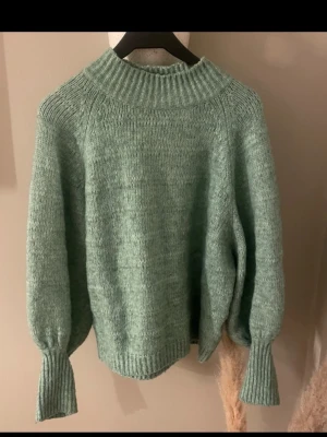 Grön stickad tröja med polokrage - Mysig stickad tröja i ljusgrönt med bred ribbad polokrage och långa, ballongformade ärmar. Tröjan har ribbade muddar vid ärmslut.