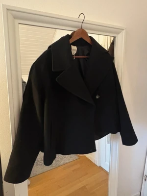 Svart Carin Wester kappa - Kort svart kappa mdd bred krage. Jackan har en  knäppning framtill och långa ärmar. Superfin och knappt använd. 38 passar S & M