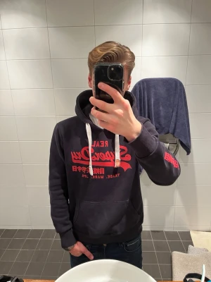 Superdry Hoodie  - Säljer denna eftertraktade hoodien från superdry. Den är mörkblå med rött tryck och hoodien är i storlek S. Den är i bra skick och priset kan diskuteras. Fråga på och be om bilder om ni vill så ses vi i dm!