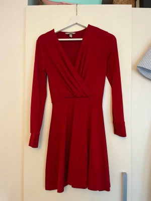 Röd omlottklänning med långa ärmar - Röd omlottklänning från H&M med v-ringning och långa ärmar. Klänningen har en mjuk och följsam passform, och är i storlek XS. 
