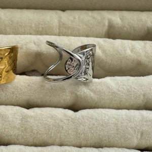 Rostfritt stål ringar (styck pris) - Säljer två snygga breda ringar med hamrad yta, en i guld och en i silver. Båda har en cool öppen design med en snirklig detalj framtill som ger dem en unik look. Perfekt för dig som gillar statement-smycken och vill sticka ut.