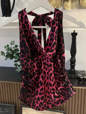 Rosa leopard halterneck topp - Rosa leopard linne med knytning i nacken. Det coola leopard mönstret täcker hela toppen. Väldigt skönt och stretchigt material. Står värken märke eller storlek men skulle säga M. Längd 50 cm. Byst: 40 cm.