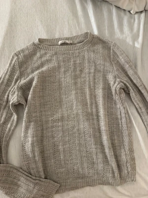  stickad tröja med hålmönster - Säljer en  stickad tröja med hålmönster och rund hals. Tröjan har långa ärmar och ribbade muddar vid ärmslut och nederkant. Perfekt för lager på lager och enkel att matcha med jeans eller kjol.