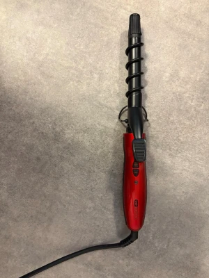 Locktång OBH Nordica röd/svart - Elektrisk locktång från OBH Nordica i röd och svart design. Handtaget är rött med svarta detaljer och har knappar för temperaturkontroll. Locktången har spiralformad stav och sladdanslutning. Ca 25-26 mm. Fungerar utmärkt. I mycket bra skick, endast testad några gånger.