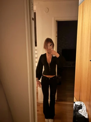 Svart blus med djup urringning - Trendig svart blus från Gina tricot med djup urringning och snygga knappar framtill. Blusen har lång ärm och fina spetsdetaljer längs kanterna. säljer pågrund av att den är för liten och har inte kvar kvitto. 