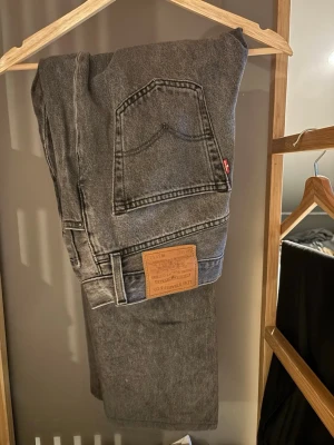 Levi's grå jeans straight fit - Grå Levi's jeans med klassisk rak passform och femficksdesign. Jeansen har en ikonisk läderpatch bak i midjan och är tillverkade i slitstarkt jeanstyg. Perfekta för en avslappnad och tidlös look.