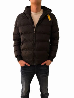 Svart dunjacka från Parajumpers - Snygg svart dunjacka från Parajumpers med huva och gul detalj vid halsen. Jackan har quiltad design, dragkedja framtill och ribbade muddar. Märkespatch på ärmen ger en exklusiv känsla. Perfekt för kalla dagar och enkel att matcha med olika outfits.