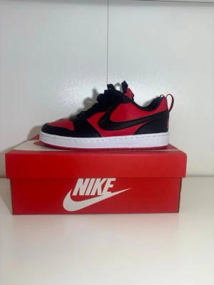 Nikes  röd och svart - Snygga Nike Jordan 1 Low sneakers i rött och svart med vit mellansula och röd yttersula. Klassisk rund tå, snörning och ikonisk Swoosh på sidan. Perfekta för dig som vill ha en streetwear-look med stil.