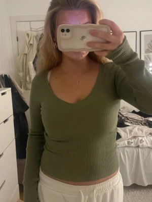 Olivgrön ribbad långärmad topp - Snygg olivgrön ribbad topp med lång ärm och v-ringning. Modellen är croppad och sitter tight, perfekt till jeans eller kjol. Mjuk och stretchig i materialet, storlek S från New Yorker