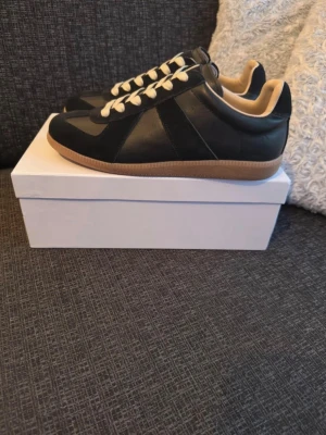 Svarta sneakers med beige sula - Stilrena svarta sneakers med beige detaljer och kontrasterande ljus sula. Skorna har snörning och en mix av skinn och mocka i materialvalen. Perfekta för dig som gillar en klassisk men modern look.
