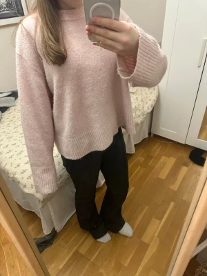 Ljusrosa stickad tröja med breda muddar - Mysig ljusrosa stickad tröja med breda ribbade muddar vid ärmslut och nederkant. Tröjan har en relaxed, loose passform och lång ärm. Perfekt för dig som gillar en enkel men söt stil.