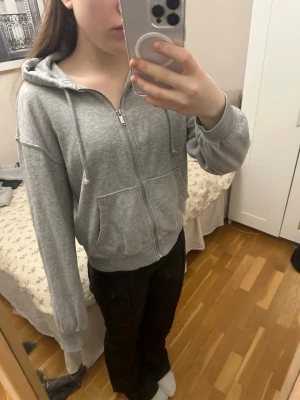Grå zip hoodie med huva - Klassisk grå zip hoodie med huva och två stora fickor framtill. Tillverkad i mjukt sweatshirtmaterial och har ribbade muddar vid ärmar och nederkant. Perfekt för en chill och avslappnad stil.
