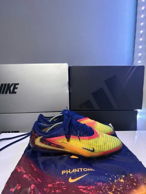 Phantom gx Elite haaland personal edition ag  - Säljer ett par  Phantom gx Elite haaland personal edition ag i storlek 42,5, skorna är köpta i unisport på nypris för ungefär 2250-3000. Skorna har en ag platta gjord för konstgräs med en snygg orange gul look. Skorna är använd max 10 gånger och är i ett bra skick. Påse och box hänger med! 