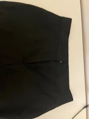 Svarta kostymbyxor med hög midja - Stilrena svarta kostymbyxor med hög midja och klassisk stängning med dragkedja, hake och knapp. Byxorna har en rak och tidlös passform som passar perfekt till en dressad look. Materialet känns mjukt och följsamt, troligtvis polyesterblandning.