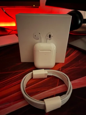 Apple AirPods  - Säljer ett par Apple AirPods med laddningsetui och laddningskabel. Snygg och stilren design i blank plast, perfekt för dig som vill ha smidiga trådlösa hörlurar till mobilen eller datorn. Kommer i originalförpackning.