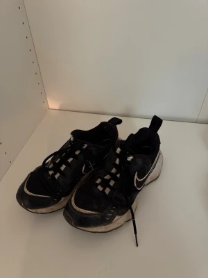 Svarta Nike sneakers med vit sula - Säljer ett par svarta Nike Air Heightd sneakers med vit sula och vit swoosh på sidan. Skorna har snörning och meshdetaljer för extra ventilation. Perfekta för dig som gillar sportig stil och vill ha bekväma skor till vardags. Lite slitna vid hälen, därav billigt pris✉️