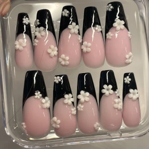 Svart och rosa lösnaglar med blommor - Säljer ett set lösnaglar med svart french tip,ljusrosa bas och vita Bloom charms. Kommer i en genomskinlig ask och du får med allt du behöver för att sätta på dom!,perfekta för att snabbt fixa snygga naglar hemma! Se storlek på sista bilden.