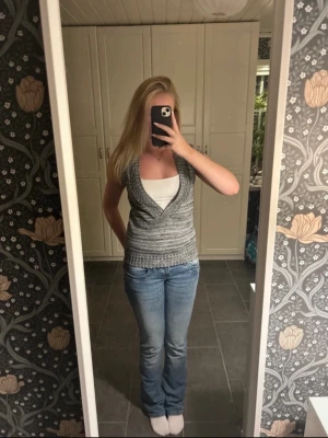 Grå stickad omlottopp - Säljer en grå stickad omlottopp med v-ringning och ribbade detaljer. Toppen har en snygg omlott-design och är perfekt att bära över ett linne. Passar dig som gillar en enkel men stilren look.