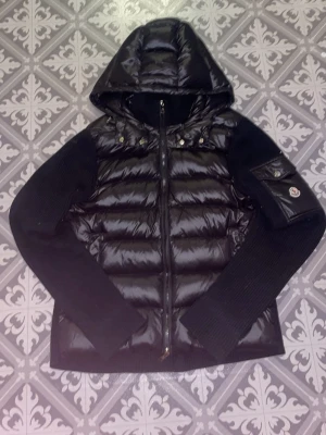 Svart dunjacka med stickade ärmar Moncler - Svart cardigan från Moncler med luva som man kan ta av. Säljer pga att den har blivit för liten