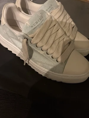 Numeris sneakers/skor - Snygga sneakers från Numeris i vitt och ljusgrått med breda snören och platt sula. Ovandelen är i canvas och detaljer i syntet. Perfekta för en clean och stilren look. Självklart äkta, köpta från officiella hemsidan för 2336 kr. Skorna är använda en gång, inga defekter eller liknande! Hör av er vid minsta fundering 