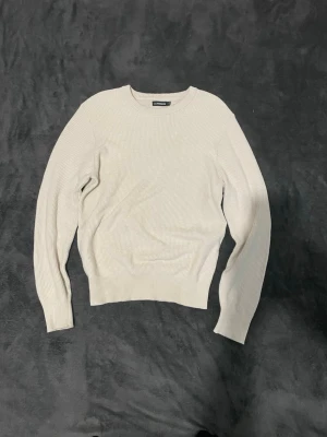 Beige stickad tröja - Snygg beige stickad tröja från j.lindeberg med rund halsringning och ribbade muddar. Tröjan har en enkel och stilren design, perfekt att matcha med jeans eller kjol. Materialet är mjukt och bekvämt, och modellen är långärmad.