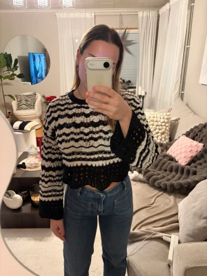 Svartvit stickad tröja med mönster - Trendig stickad tröja i svart och vitt med vågigt mönster och hålstickade detaljer. Tröjan har rund halsringning, långa ärmar och en något croppad passform. Perfekt för dig som gillar en unik och cool stil.