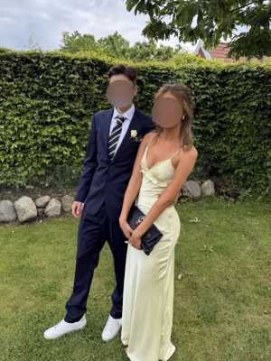 Ljusgul balklänning bröllopsklänning  - Säljer en elegant ljusgul långklänning i satinliknande material som endast används under en kväll. Klänningen har smala axelband, v-ringning och en snygg öppen rygg med fina detaljer. Överraskande skön att bära och är tyngre i materialet så faller väldigt fint på kroppen. Perfekt för bal eller bröllop!! ✨✨ jag är 175, bar små klackar på balen och har sytt upp klänningen runt 3 cm. Dessutom har jag sytt ihop v tingningen men den är enkel att sprätta upp i behov. 