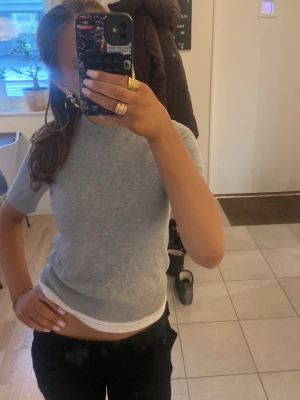 Grå ribbad kortärmad topp - Snygg grå ribbad topp med korta ärmar och rund hals. Perfekt att styla med jeans eller kjol för en enkel och clean look. Materialet känns mjukt och stretchigt, vilket gör den bekväm att bära hela dagen.