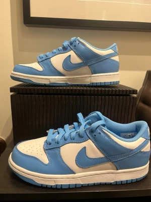 Nike Dunk Low blå och vita sneakers - Säljer ett par Nike Dunk Low i den populära UNC Blue / vita färgkombinationen. Stilrena och lätta att matcha, passar både vardag och streetwear.  Skorna är oanvända!