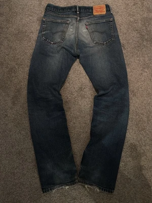 Levi's archive vintage  - Klassiska blå Levi's jeans med straight fit. Jeansen har en mörk tvätt med slitningar  och den ikoniska läderpatchen bak i midjan. Tillverkade i tålig bomullsdenim och har den typiska röda Levi's-taggen på bakfickan. Inga defekter. Osäker på modellen. Eftersom  lappen har blivit ”utsuddad”. Skriv vid frågor eller intresse.