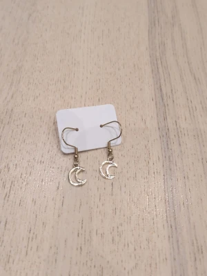Guldiga örhängen med månhänge i rostfritt stål  - Säljer ett par snygga örhängen i guldfärgad metall med hängande månar. De har enkel krok och en stilren, trendig design som passar perfekt till dig som gillar detaljer med lite mystisk vibe. Perfekt accessoar för att lyfta din look.