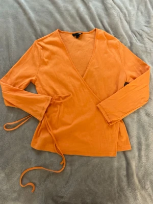 Orange omlottopp med trekvartsärmar - Snygg orange omlottopp med trekvartsärmar och knytband i midjan. Toppen har en djup v-ringning och är tillverkad i mjukt bomullstyg. Perfekt för dig som vill ha en färgstark och trendig look. Står storlek 40/42 men skulle säga mer M❤️